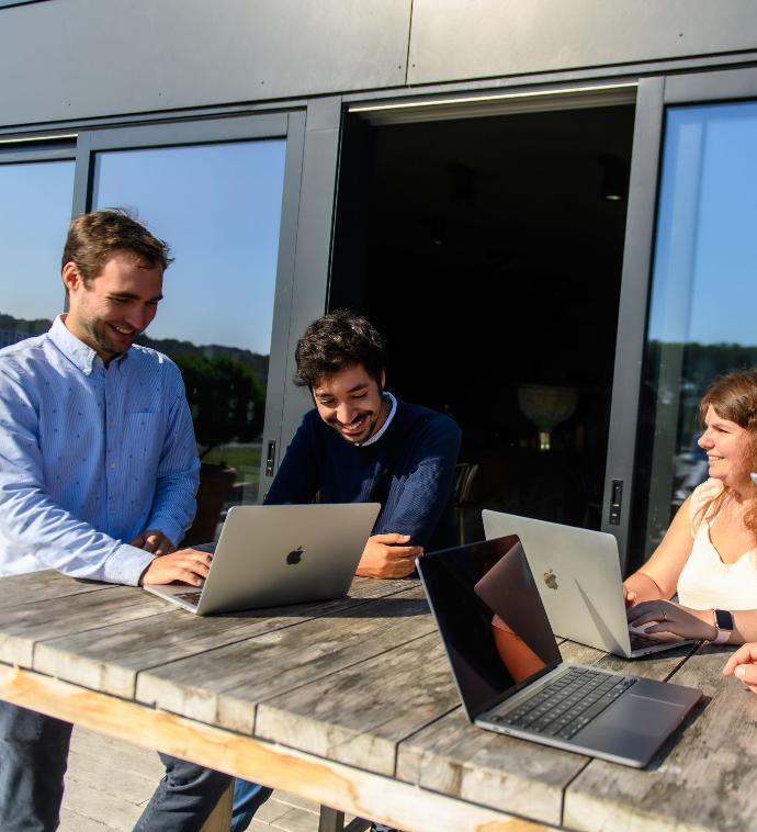 tres empleados de la empresa de servicios discutiendo puntos como Crear su sitio web completo en Odoo, están todos en una mesa de reuniones con 3 portátiles Macbook pro.