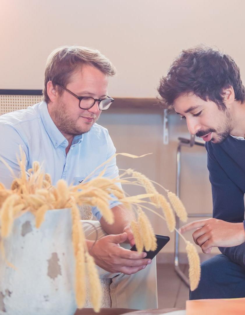 foto de Ilias Bitar y Brieuc Thoumsin hablando de su potencial digital con la ayuda de nuestros expertos en torno a un teléfono móvil sentados en sillas con una hermosa planta en primer plano.